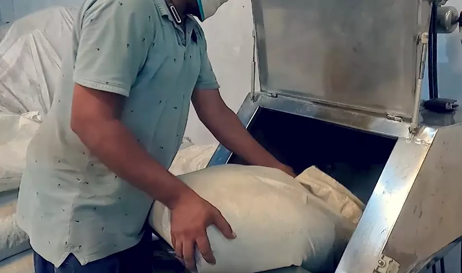 man emptying a sack of some raw material into a machine funnel